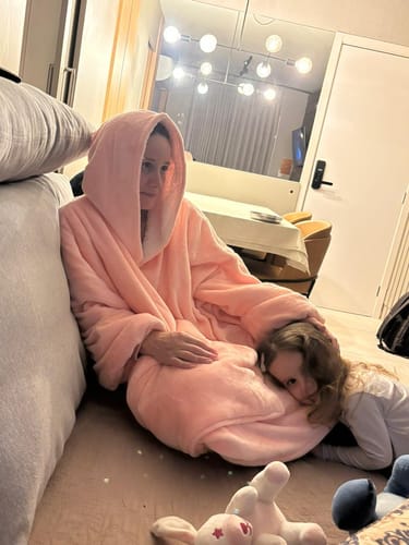 Cliente vestindo o Sleepo Rosa com capuz enquanto relaxa no chão da sala com uma criança.