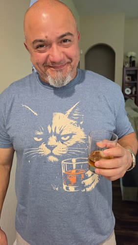 Customer wearing the blue Sourpuss Whiskey Cat Grunge T-Shirt while holding a glass of whiskey.