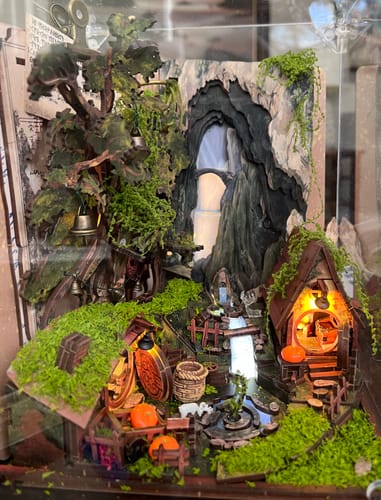 Customer's Whispering Hollow Miniature House Kit built into an intricate, mossy scene with a glowing cottage and waterfall.