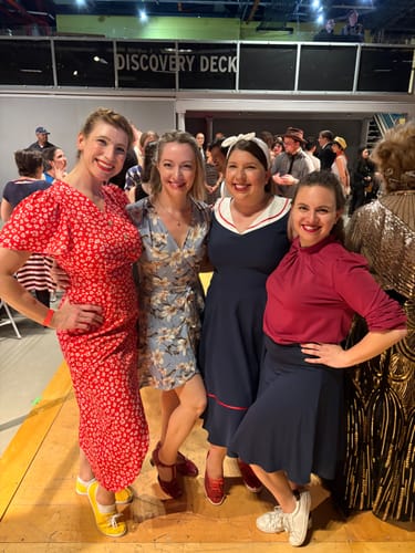 Customer on the left in the red floral V-neck dress, posing with friends at a vintage dance event.
