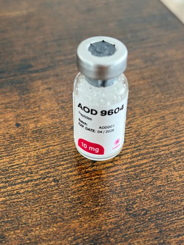 Cliente muestra el vial del Peptido AOD 9604 de 10 mg sobre una mesa de madera.