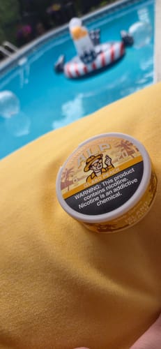 Customer's tin of Drifters Island Peach pouches resting on a yellow surface next to a swimming pool.