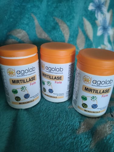 Recensore mostra tre flaconi di Mirtillase Forte con il tappo arancione su una coperta.