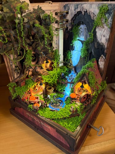 Reviewer's assembled Whispering Hollow Miniature House Kit, showing a lit-up village with a detailed waterfall and tiny houses.