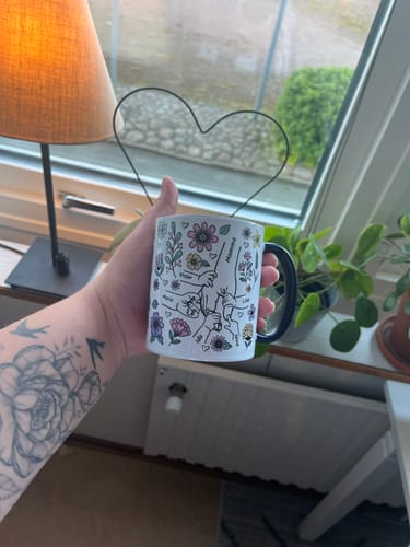 Kund håller i sin Kärleksmugg med en tecknad design av händer och blommor.