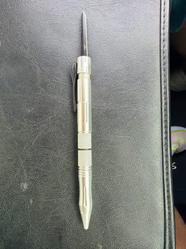 Customer's silver VT Tactical OTF Pen Knife shown with the blade fully extended on a black surface.