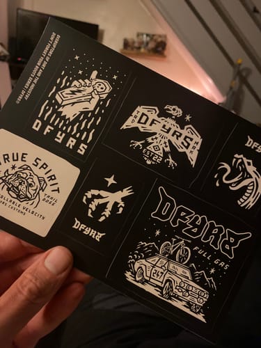 Customer holding a black Lucky Dip Sticker Sheet featuring several white graphic designs.