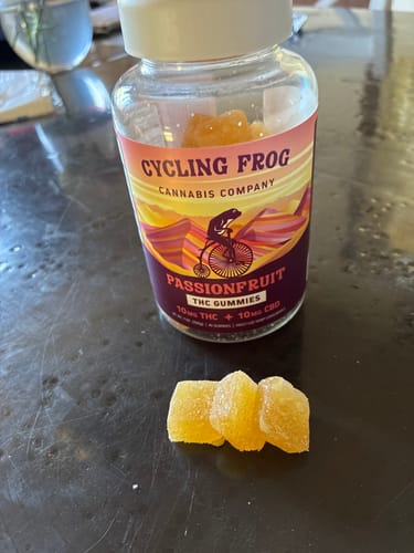 Customer's bottle of Passionfruit Gummies with three yellow, sugar-coated gummies on a dark table.