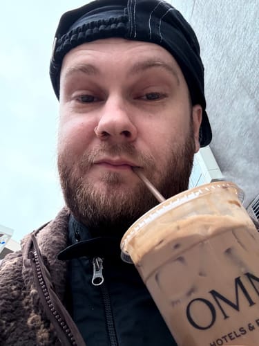 Close-up of a customer wearing the black Big Camp Hat backwards while holding a drink.