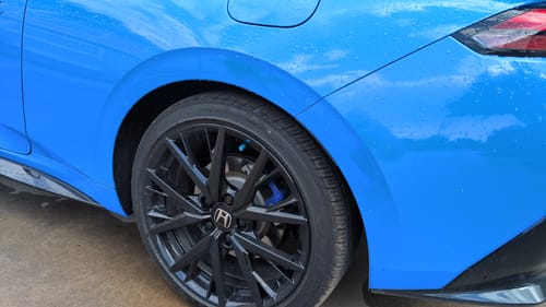 Reviewer's teal valve stem cap installed on the wheel of a blue car.
