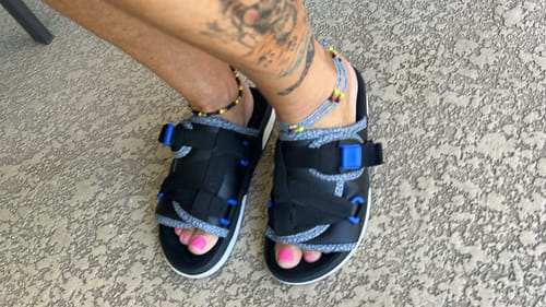 Customer's feet in black Original Dracoslides, showing the adjustable straps and blue accents.