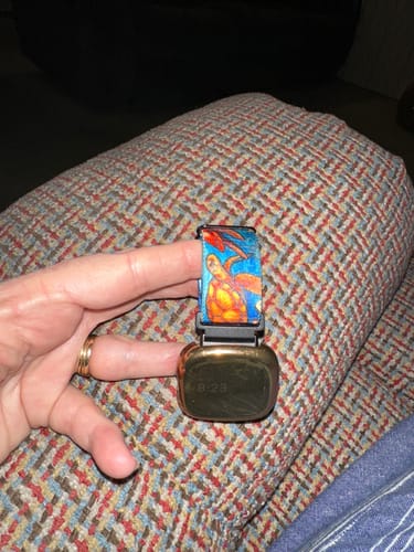 Close-up of a reviewer's hand holding a smartwatch with the colorful Turtle Package Watch Band.