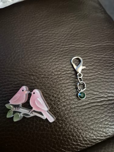 Reviewer's bird keychain in two separate pieces: the pink bird charm and the metal clasp with a green gem.