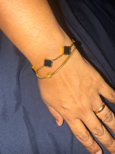 Reviewer wearing the gold Forever Knot Bracelet on their wrist, stacked with a black charm bracelet.