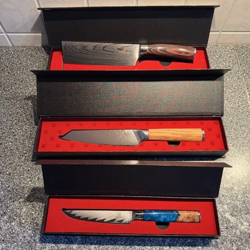 Ein Kunde zeigt drei verschiedene Premium-Küchenmesser aus der Mystery Box S in ihren offenen Geschenkboxen.
