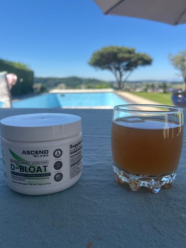 Reviewer's D-BLOAT tub and a glass of the prepared drink on a table by a sunny pool.