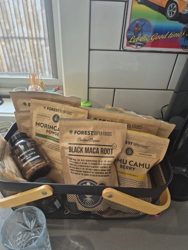Customer's Certified Organic Black Maca Powder in a pouch and bottle, displayed in a basket with other superfoods.