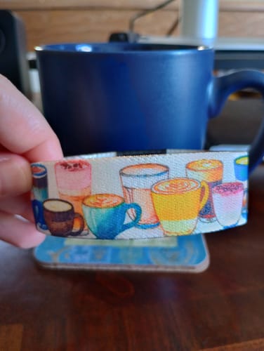 Reviewer holding the colorful Mug Life Bracelet in front of a blue coffee mug on a desk.