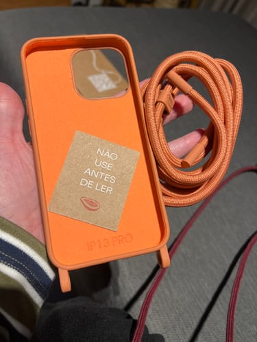 Consumidor segurando a capa para celular Cordinha Odara Pêssego com sua alça de corda correspondente.