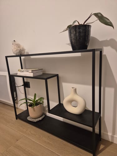Reseña de un cliente del arrimo Zeta de metal negro, instalado contra una pared con plantas y objetos decorativos.