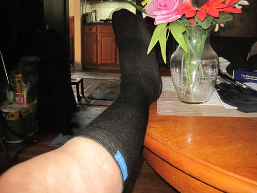 Customer shows the fit of the black Eucalyptus Lyocell Compression Socks while resting their leg on a table.
