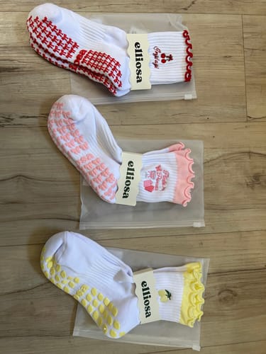 Reviewer displays three pairs of Pilates Princess socks with cute non-slip grips and frilly cuffs in red, pink, and yellow.