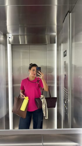 Cliente tirando uma selfie no espelho do elevador, usando a Cordinha Nora marrom café para segurar o celular.