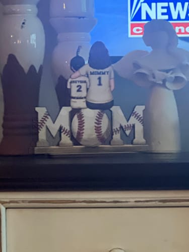 Customer's personalized wooden plaque showing mom and child figures in baseball jerseys, resting on the word 'MOM'.