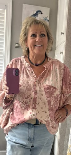 Reviewer in a mirror selfie wearing the pink patterned Blush Beauty Top tucked into jeans.