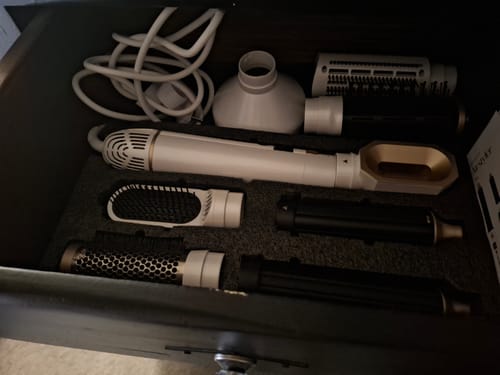 Klant toont de SANSBEAUTÉ® 8-IN-1 AIRSTYLER met alle opzetstukken in een opberglade.