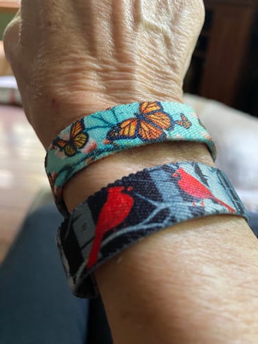 Reviewer's wrist wearing two fabric bracelets, one with butterflies and the other with red cardinals.