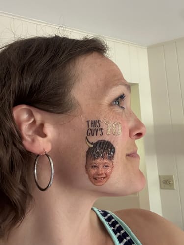 Reviewer wearing a custom photo tattoo on her cheek. The tattoo shows a boy's face and says 'THIS GUY'S 10'.