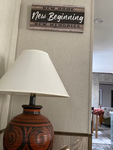Customer's New Home, New Beginning sign hanging on a textured wall above a lamp in their home.