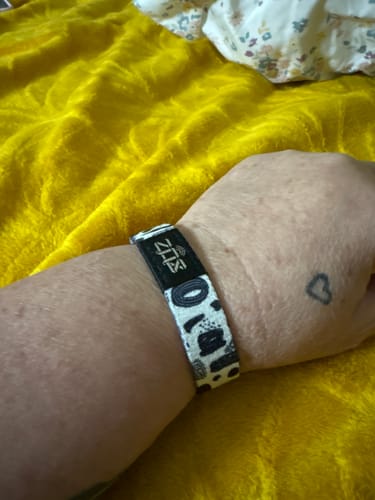 Customer wearing the black and white patterned Let It Go Bracelet on their wrist against a yellow background.