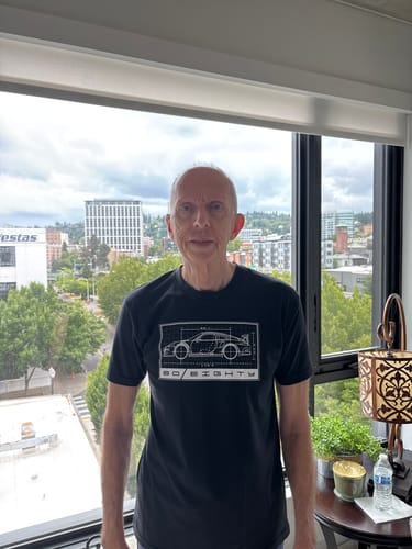 Customer wearing the black 80Eighty® GT3RS Specs Shirt while standing indoors in front of a window.