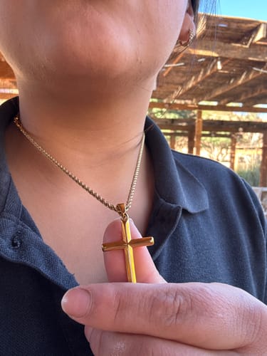 Cliente mostrando de cerca el colgante Crucifix Pendant Oro que lleva puesto.
