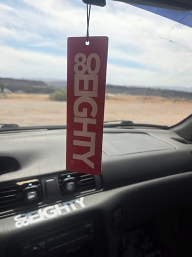 Customer's red 80Eighty air freshener hanging from the rearview mirror inside a car.