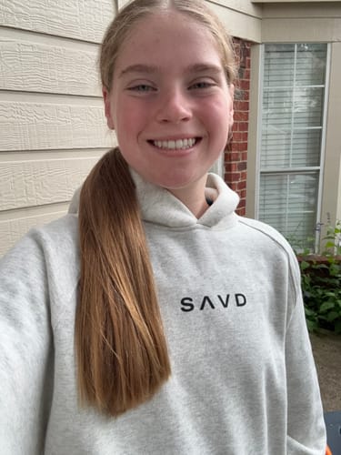 Reviewer smiling in the light gray Loved by God Oversized Hoodie, with the SAVD logo visible on the chest.