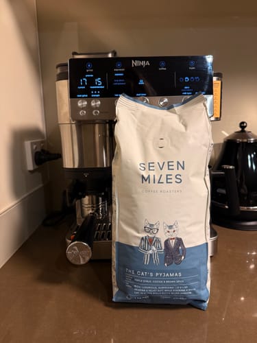 Customer's bag of The Cat's Pyjamas coffee beans on a kitchen counter in front of a coffee machine.