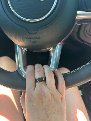 Customer's hand on a steering wheel, wearing a black silicone ring with a gold-toned heart frame.