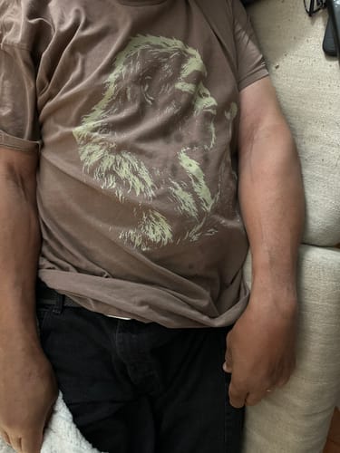 Customer wearing the brown garment-dyed Blowing Wishes T-Shirt while sitting on a couch.