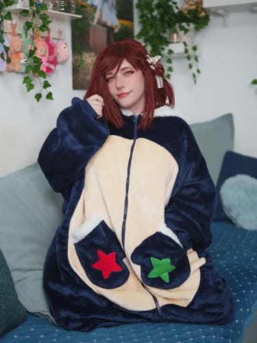 Reviewer sitting on a couch wearing the oversized OLAOLA wearable blanket, with hands in the mitten-shaped pockets.