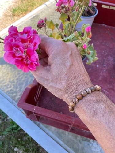 Client portant le Bracelet Jaspe Paysage au poignet à côté d'une fleur rose.
