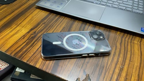 Customer's Anti Yellow Magsafe Clear Case on an iPhone, shown on a wooden desk next to a laptop.