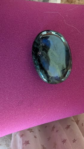Close-up of the reviewer's dark, polished monthly crystal from the VIP Crystal Club on a magenta surface.