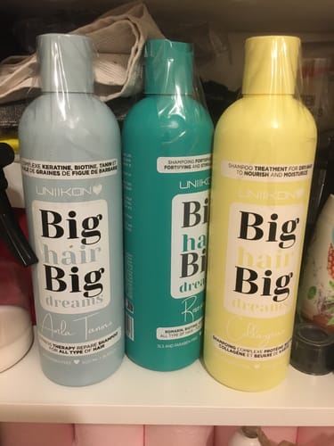 Une cliente montre trois bouteilles de shampoing de la gamme, y compris le shampoing au romarin, alignées sur une étagère.