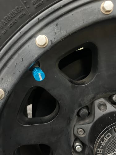 Close-up of a customer's teal 80Eighty Valve Stem Cap on a black wheel.