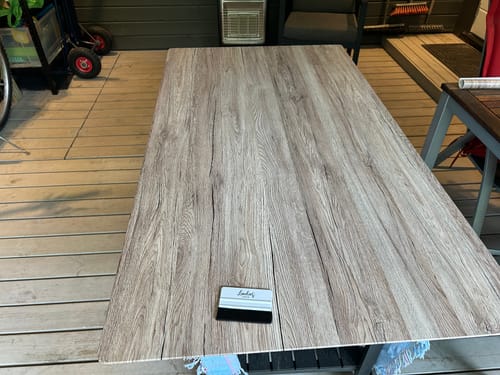 En kunde som påfører Sanremo Eik Natur kontaktplast på en bordplate. En skrape ligger på overflaten.