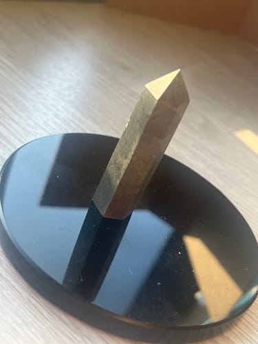 Reviewer's hematite crystal point standing on a reflective black display stand on a wooden surface.