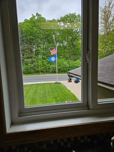 Customer's old style Minnesota flag flying on a flagpole outside a window, below an American flag.